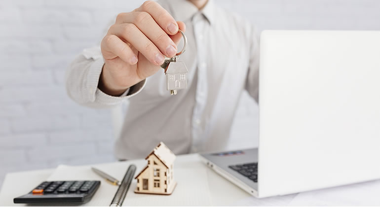 Homem mostrando chave de casa na frente de um notebook